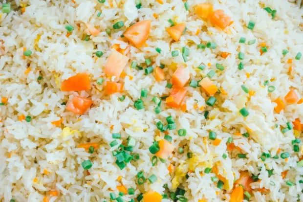 Arroz de festa decorado com pedaços de tomate, cenoura, cebolinha e ovos, formando um prato colorido e saboroso.