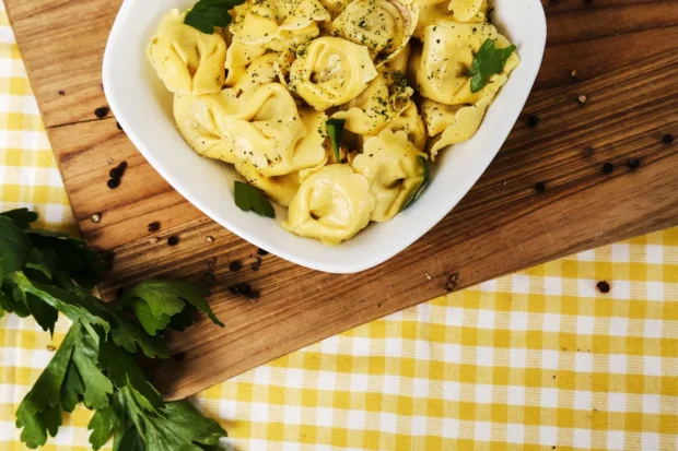 Prato de capeletti caseiro temperado com ervas frescas, servido em uma tigela branca sobre uma tábua de madeira com detalhes rústicos e folhas de salsa ao lado.