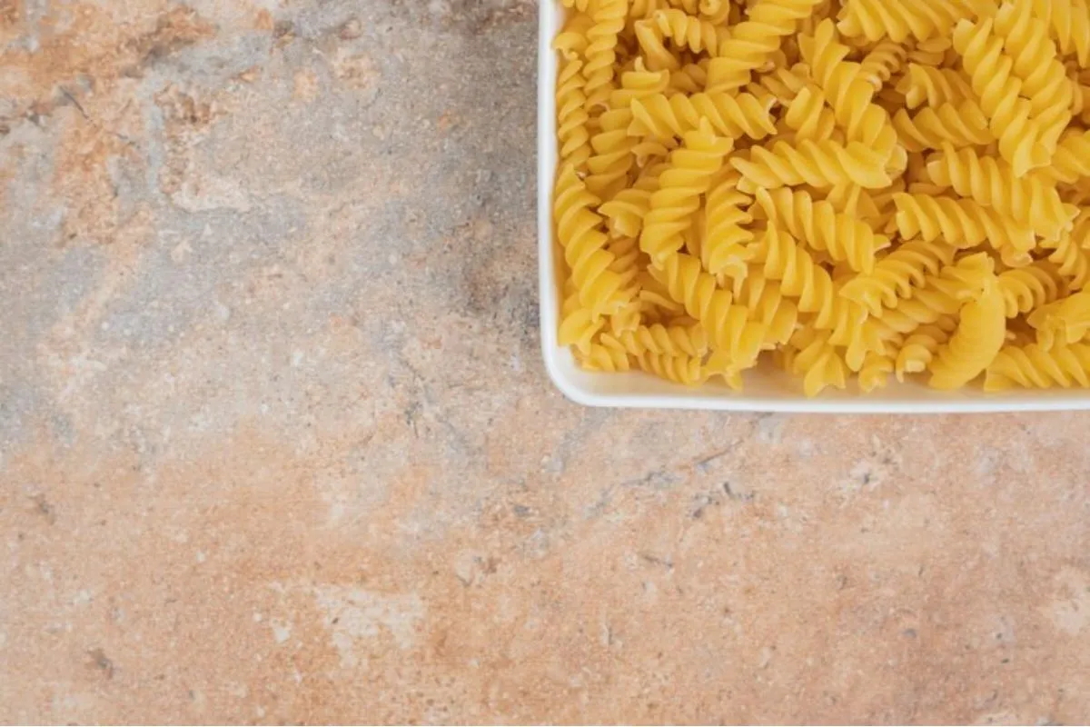 Macarrão fusilli cru em uma travessa branca sobre uma superfície de pedra.