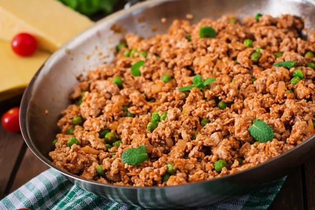 Carne moída refogada com ervilhas e hortelã em uma frigideira de aço inox, pronta para servir.