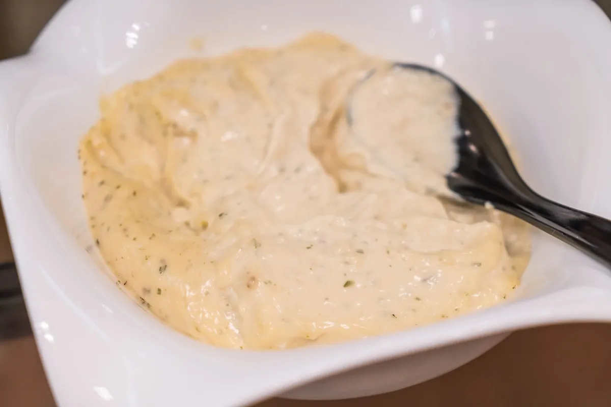 Molho aioli caseiro em uma tigela branca com colher preta, destacando sua textura cremosa e temperos.