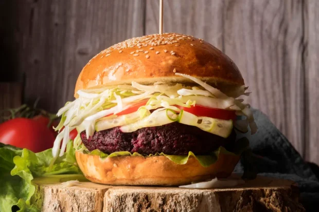 Hambúrguer vegetariano com pão brioche, alface, repolho, tomate e um suculento hambúrguer de beterraba, servido em um cenário rústico.