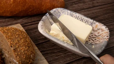 Barra de manteiga caseira em um prato rústico, acompanhada de pães artesanais sobre uma mesa de madeira.