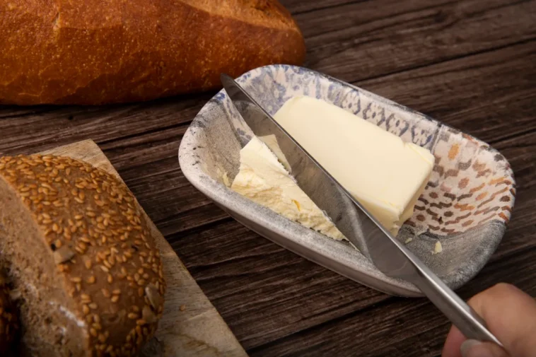 Barra de manteiga caseira em um prato rústico, acompanhada de pães artesanais sobre uma mesa de madeira.