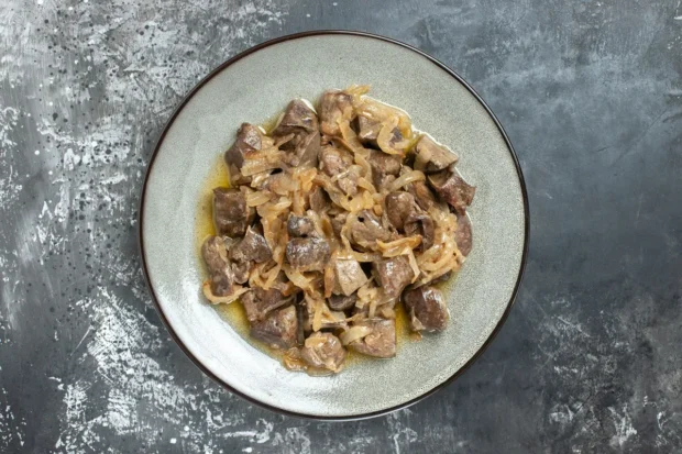 Prato de moela de frango cozida com cebola caramelizada, servido em uma louça rústica sobre uma superfície texturizada cinza.