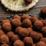 Trufas de chocolate cobertas com cacau em pó dispostas em uma bandeja sobre uma mesa de madeira.