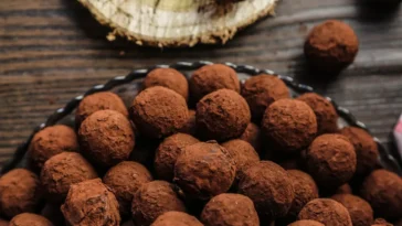 Trufas de chocolate cobertas com cacau em pó dispostas em uma bandeja sobre uma mesa de madeira.