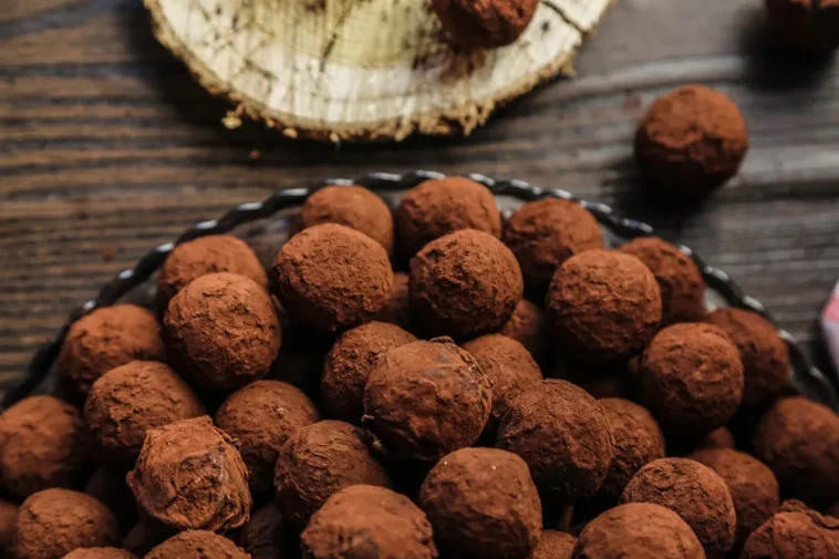 Trufas de chocolate cobertas com cacau em pó dispostas em uma bandeja sobre uma mesa de madeira.