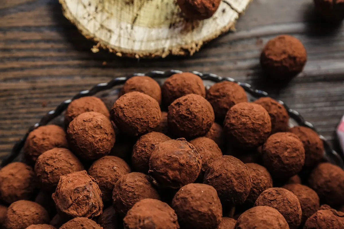 Trufas de chocolate cobertas com cacau em pó dispostas em uma bandeja sobre uma mesa de madeira.