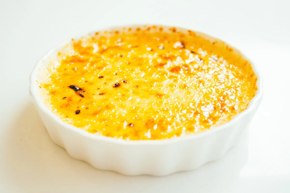 Suflê de chuchu servido em um ramequim branco, com a superfície dourada e crocante, apresentando um aspecto cremoso e apetitoso.
