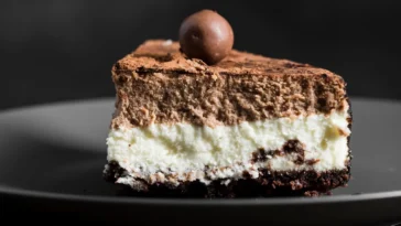 Fatia de bolo de prestígio com camadas cremosas de chocolate e coco, polvilhada com cacau e decorada com uma trufa de chocolate no topo.