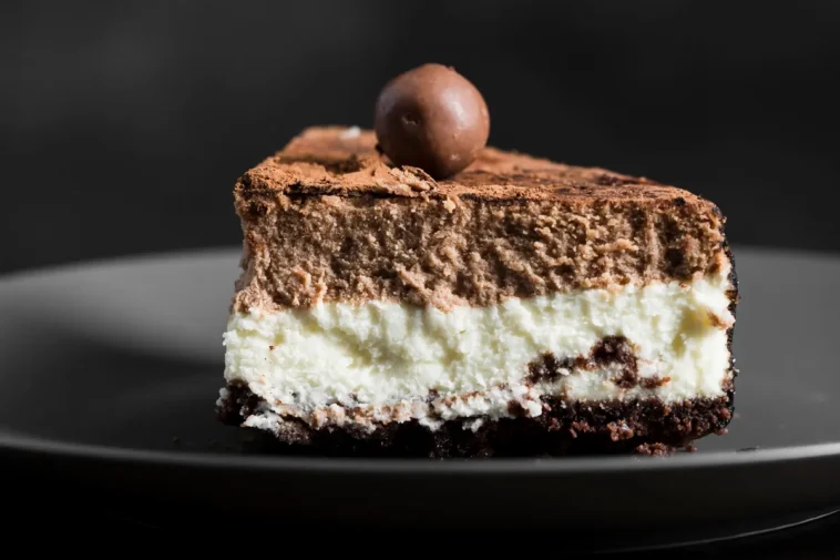 Fatia de bolo de prestígio com camadas cremosas de chocolate e coco, polvilhada com cacau e decorada com uma trufa de chocolate no topo.