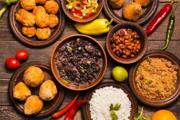 Variedade de pratos típicos da culinária brasileira, incluindo feijoada, farofa, arroz, bolinhos fritos e pimenta, servidos em louça rústica sobre mesa de madeira.