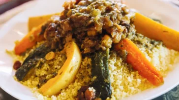 Prato de cuscuz marroquino servido com legumes assados e carne ao molho, realçando a riqueza dos temperos típicos da culinária árabe.