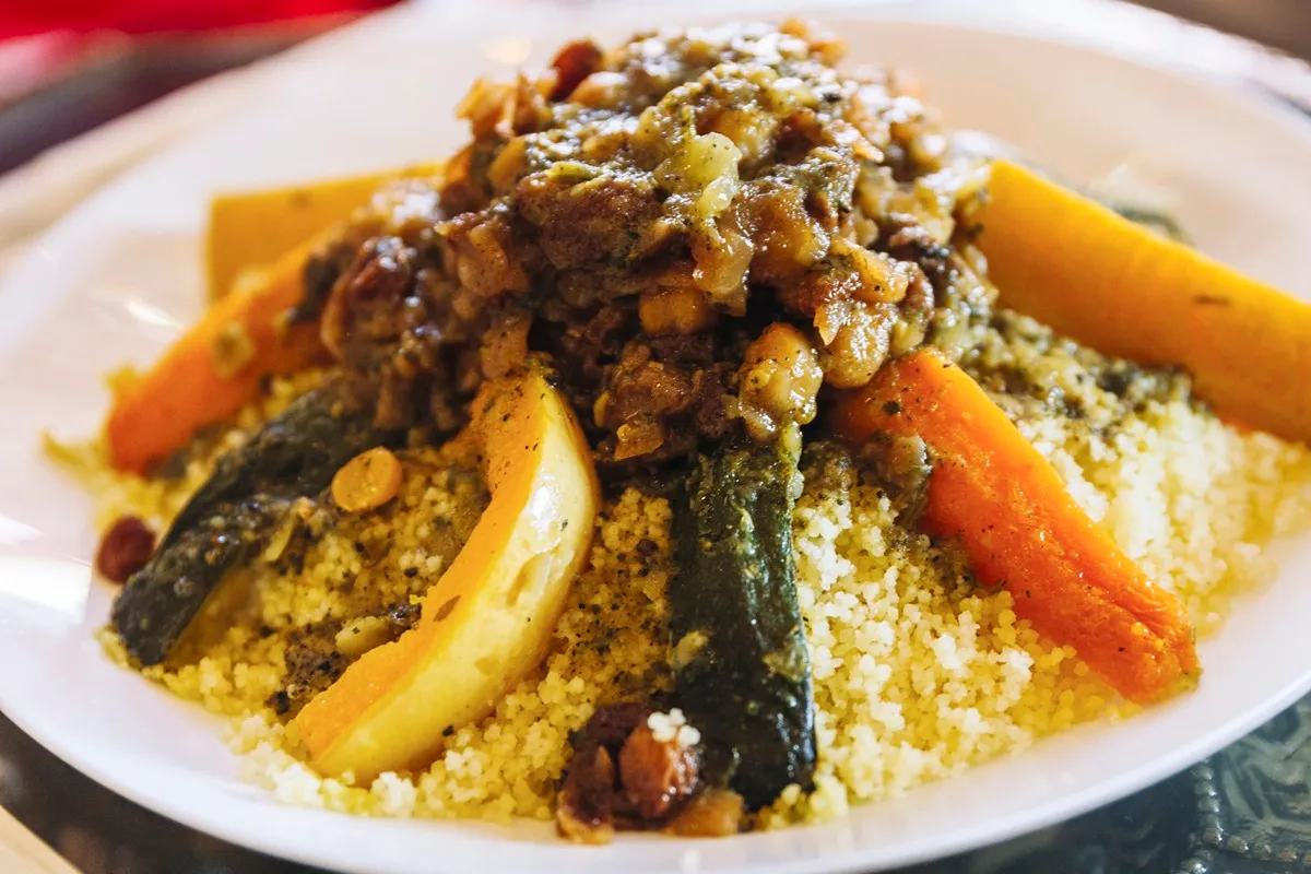 Prato de cuscuz marroquino servido com legumes assados e carne ao molho, realçando a riqueza dos temperos típicos da culinária árabe.