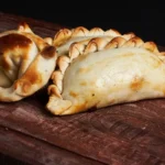 Empanadas argentinas douradas e assadas, com bordas trançadas, servidas sobre uma tábua de madeira rústica.