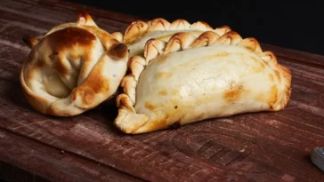 Empanadas argentinas douradas e assadas, com bordas trançadas, servidas sobre uma tábua de madeira rústica.