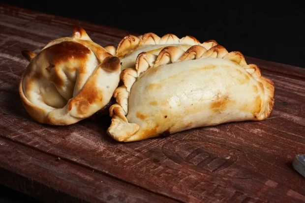 Empanadas argentinas douradas e assadas, com bordas trançadas, servidas sobre uma tábua de madeira rústica.