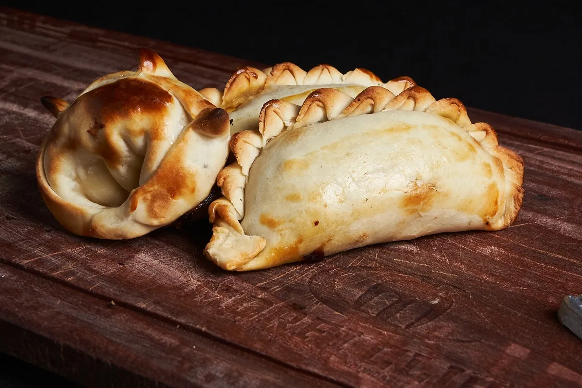 Empanadas argentinas douradas e assadas, com bordas trançadas, servidas sobre uma tábua de madeira rústica.