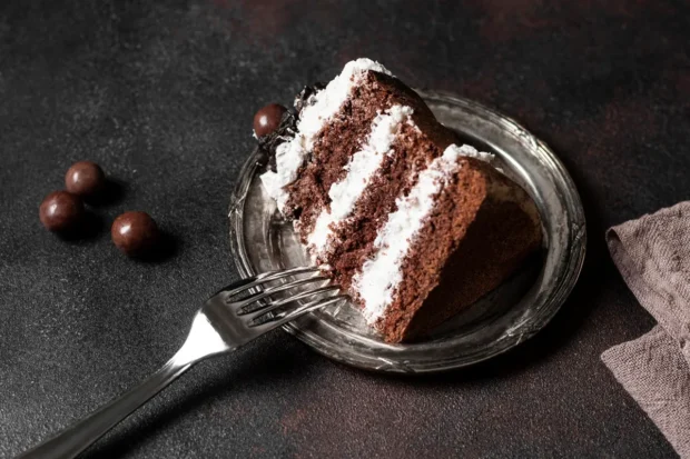 Fatia de bolo de prestígio servida em um prato rústico, com camadas de bolo de chocolate e recheio cremoso de coco, acompanhada por bombons de chocolate.