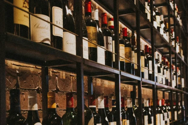 Garrafas de vinho armazenadas em prateleiras metálicas em uma adega com parede de tijolos aparentes