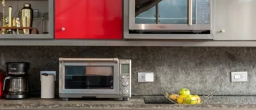 Cozinha moderna com armários coloridos, micro-ondas, forno elétrico, cafeteira e fruteira com maçãs sobre bancada de granito.