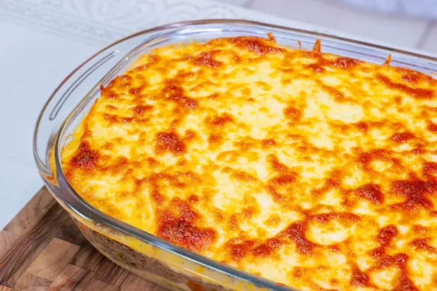 Travessa de vidro com escondidinho de carne de sol ao forno, coberto com queijo gratinado dourado.