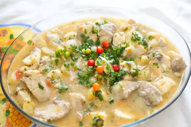 Mojica de pintado servida em travessa de vidro, com pedaços suculentos de peixe, caldo cremoso, cheiro-verde e pimentas coloridas no centro.
